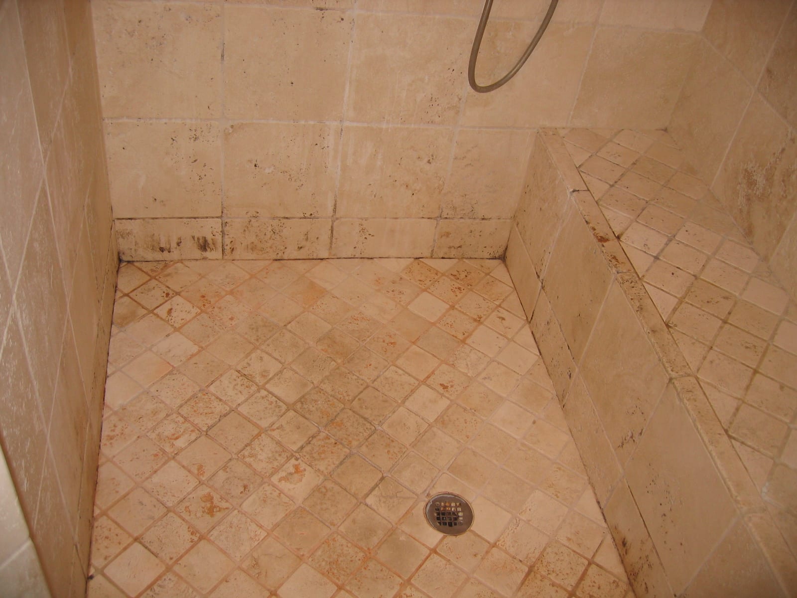 Travertine shower before: scale, soap scum and dark staining on the stone